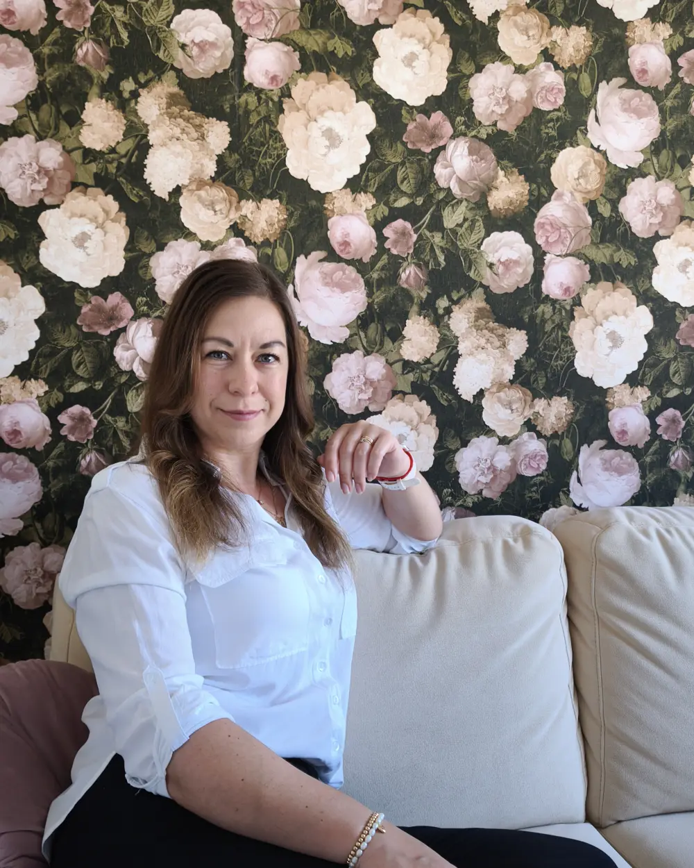 Tatiana Müller sitzt vor einer Blumentapete auf einem Sofa.